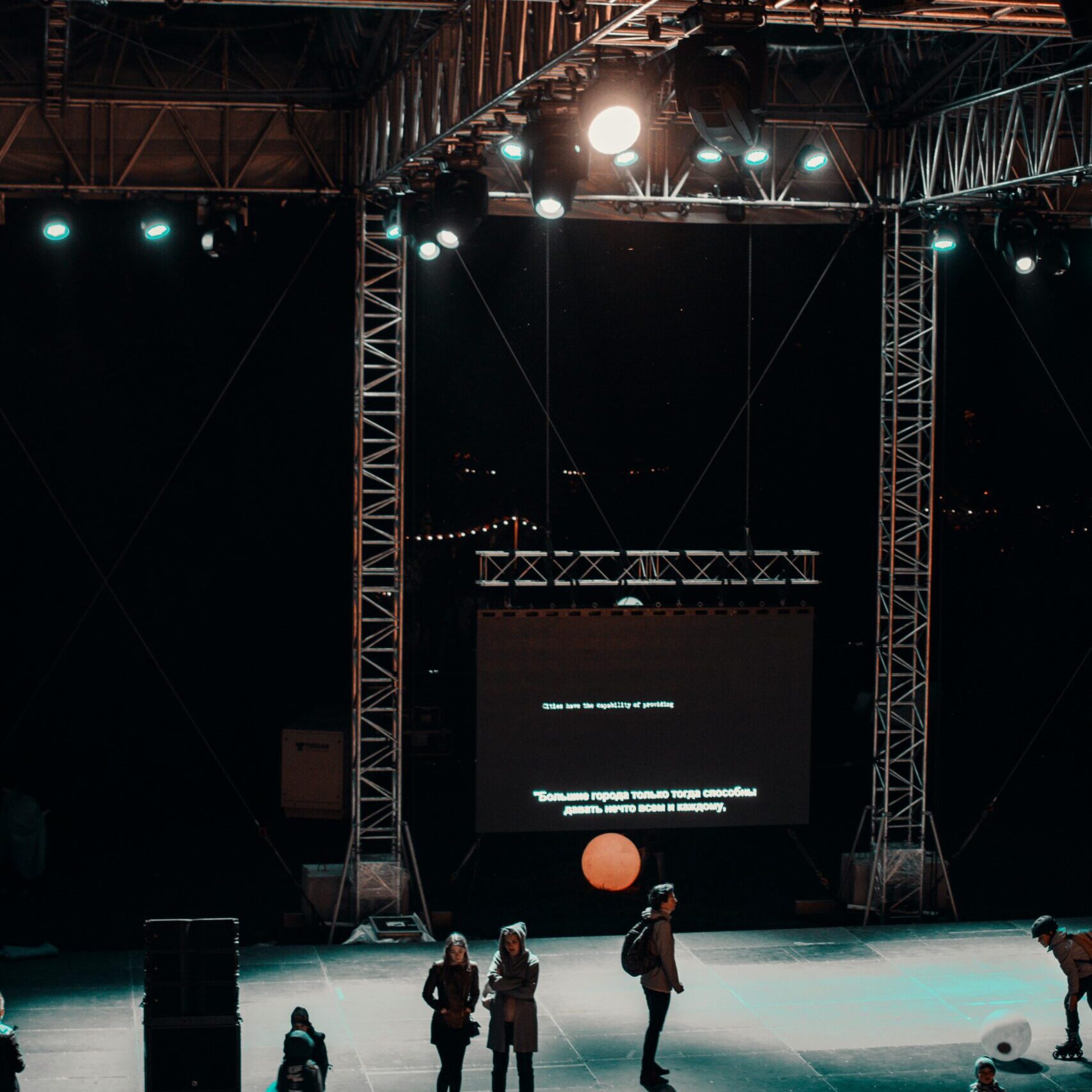 Home A vibrant nighttime stage setup with a crowd, lights, and a projected screen creating a lively atmosphere.