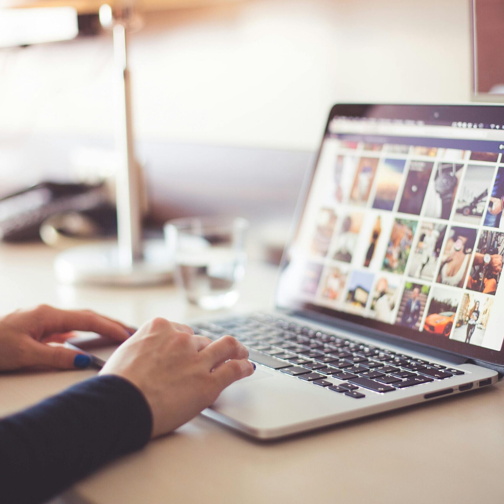 Home Close-up of hands typing on a laptop with an image gallery open on the screen.