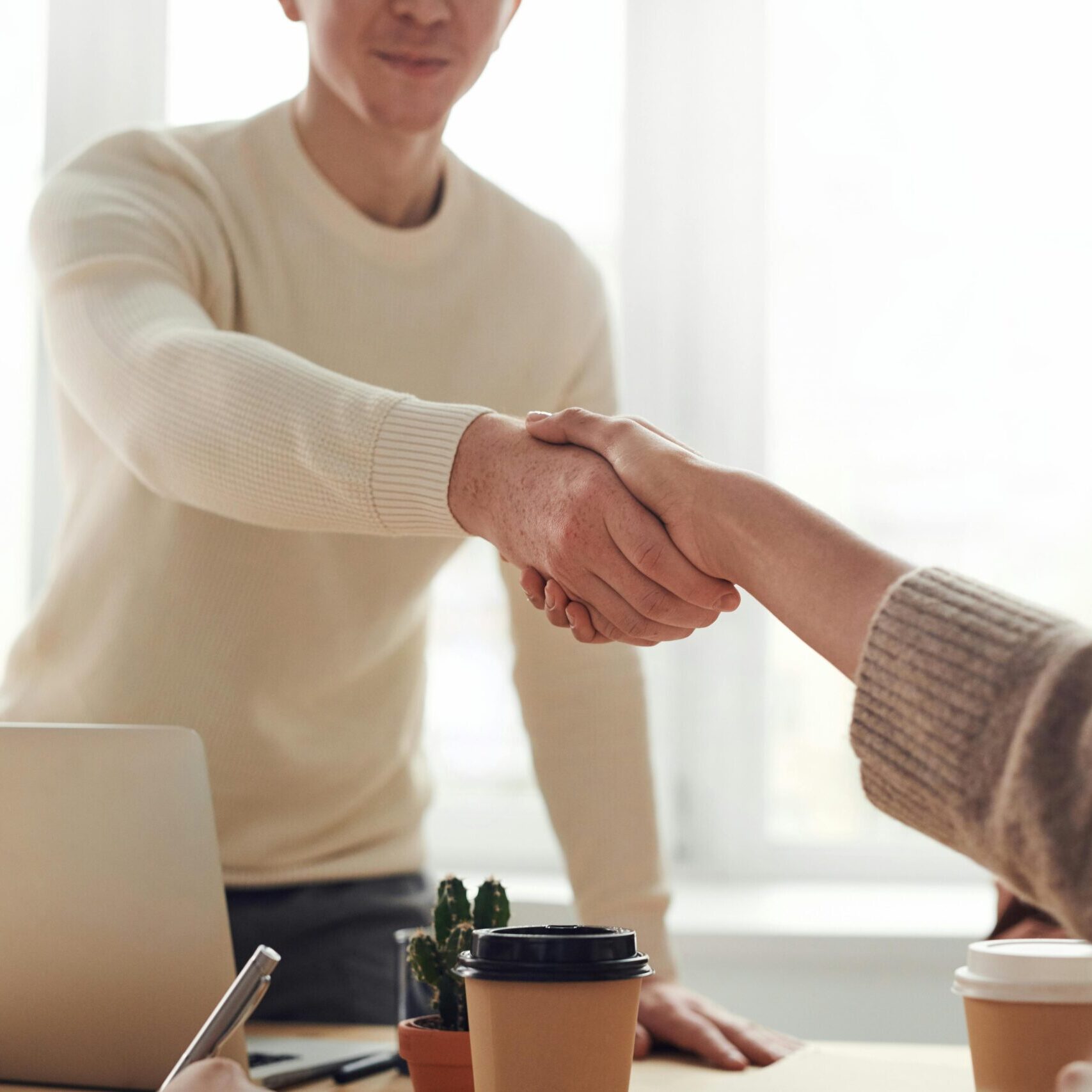 Home Close-up of professionals shaking hands over coffee in a modern office.