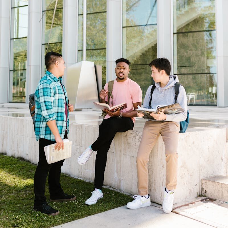 Home Three college students having a discussion outdoors near a modern campus building.