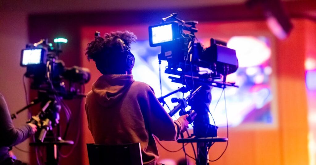 Back view of a videographer operating a camera at a live event, focusing on a vibrant indoor setup.