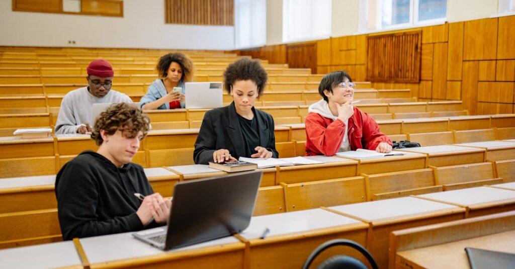 Group of college students studying together in a classroom, focused on learning with laptops and books.