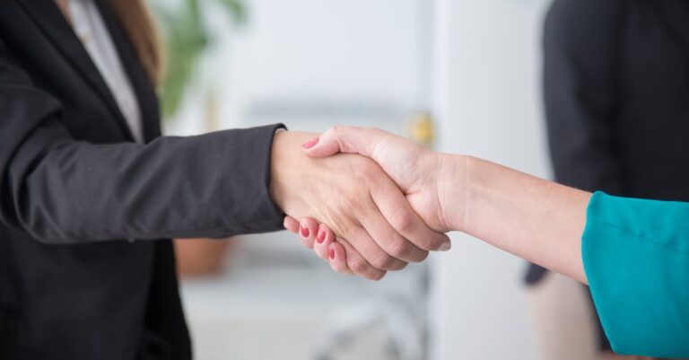 Close-up of a professional handshake between businesswomen in an office environment.
